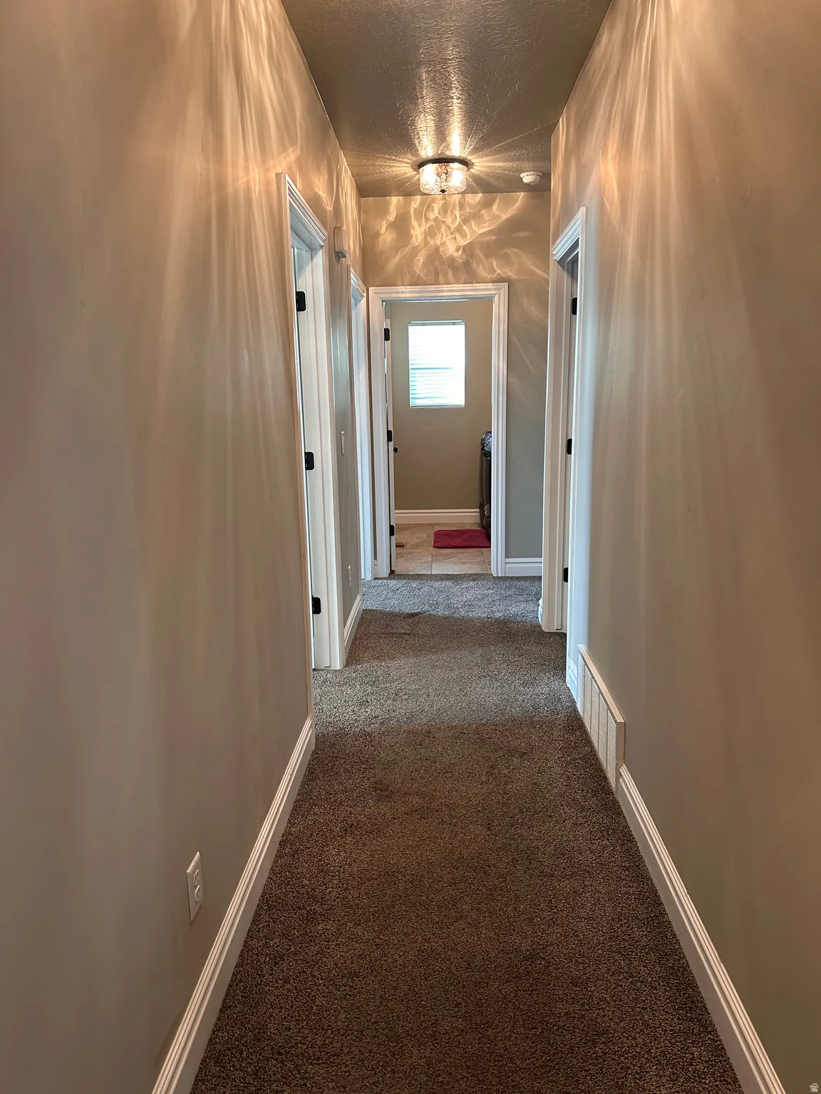 Hallway with dark carpet and a textured ceiling