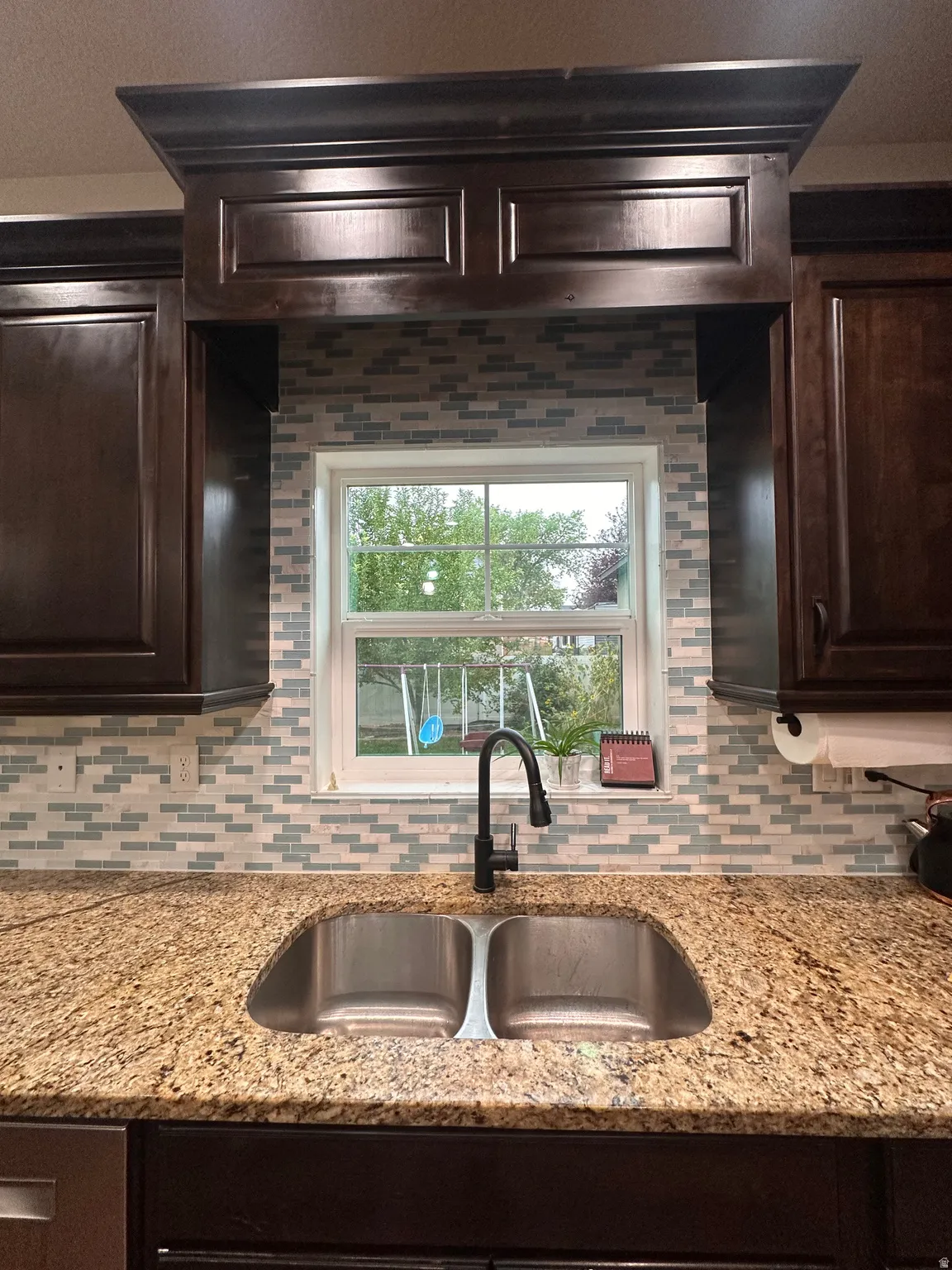 Kitchen featuring dark wood finish cabinetry, light stone countertops, and backsplash
