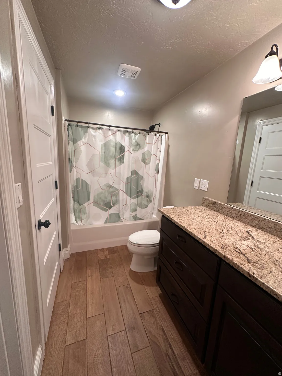 Full bath with vanity, dark wood finished floors, shower / bathtub combination with curtain, and a textured ceiling