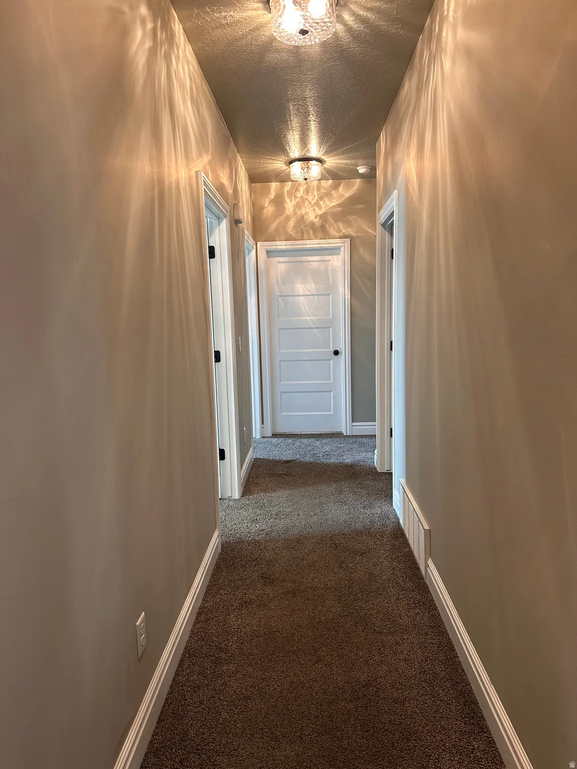 Corridor featuring dark colored carpet and a textured ceiling