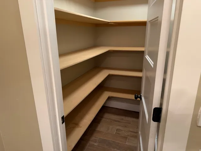 Walk-in pantry featuring abundant L-shaped shelving, solid panel door with matte black hardware, tile flooring, and neutral wall tones