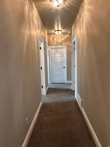 Corridor featuring dark colored carpet and a textured ceiling