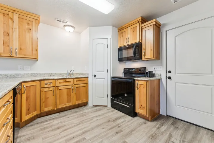 Kitchen with black appliances, light stone countertops, a textured ceiling, and light wood-style flooring