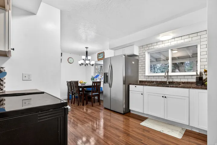 Kitchen featuring stainless steel fridge, backsplash, white cabinets, dark wood-style flooring, and a textured ceiling