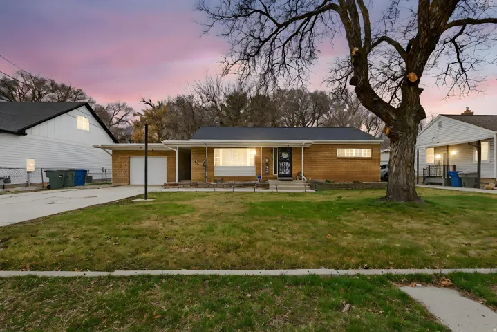 View of front facade with brick siding, a front yard, a garage, driveway, and covered porch