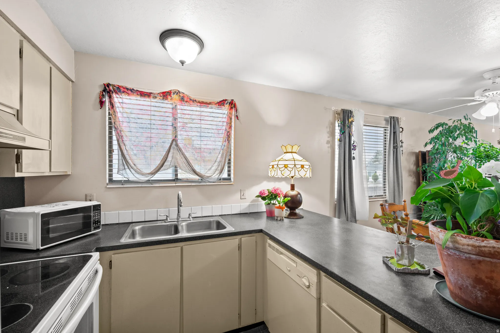 Kitchen with cream cabinetry, dark countertops, white appliances, and ceiling fan