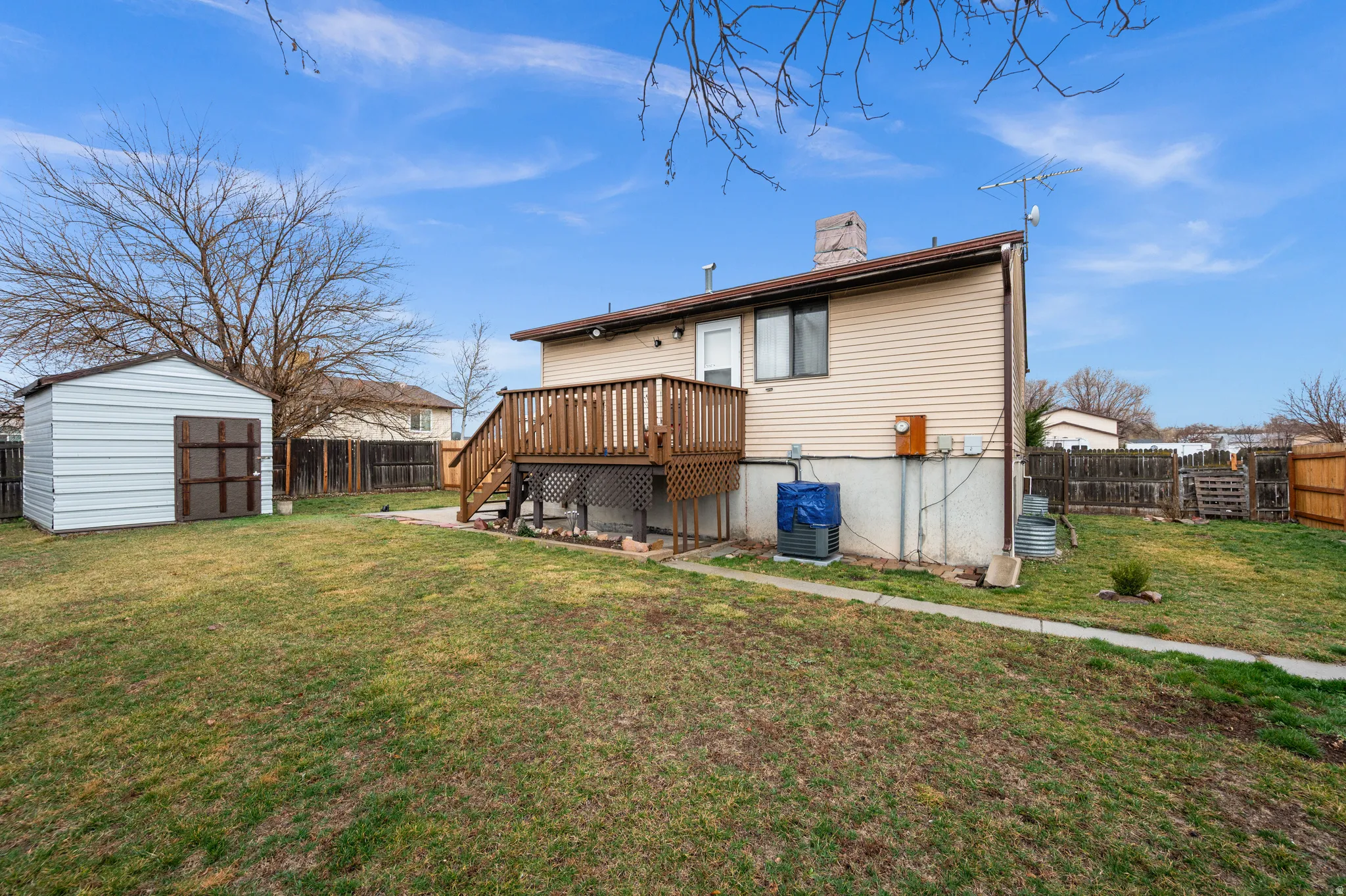 Back of property featuring a fenced backyard, a chimney, a deck, and a storage shed