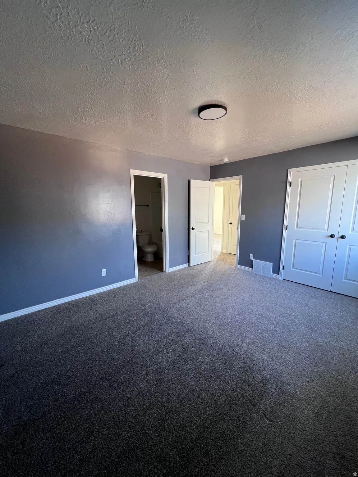 Unfurnished bedroom with a closet, ensuite bathroom, carpet, and a textured ceiling