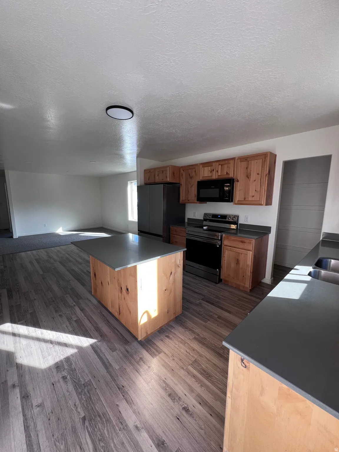 Kitchen with stainless steel range with electric cooktop, dark wood-type flooring, black microwave, freestanding refrigerator, and dark countertops