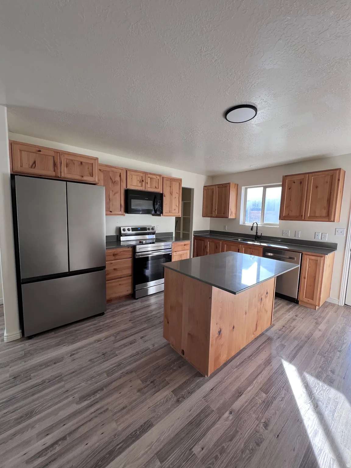 Kitchen with stainless steel appliances, dark countertops, a kitchen island, a textured ceiling, and dark wood-type flooring