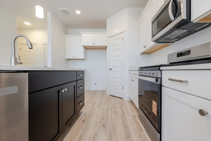 Modern kitchen featuring stainless steel appliances, two-tone cabinetry, wood-finish flooring, and recessed lighting