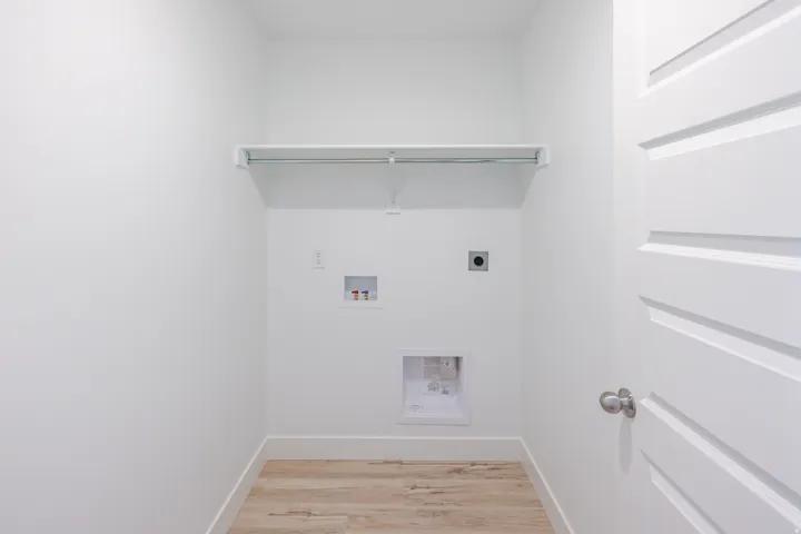 Laundry area featuring wood-finish flooring, a white shelving unit, and a built-in hanging rod