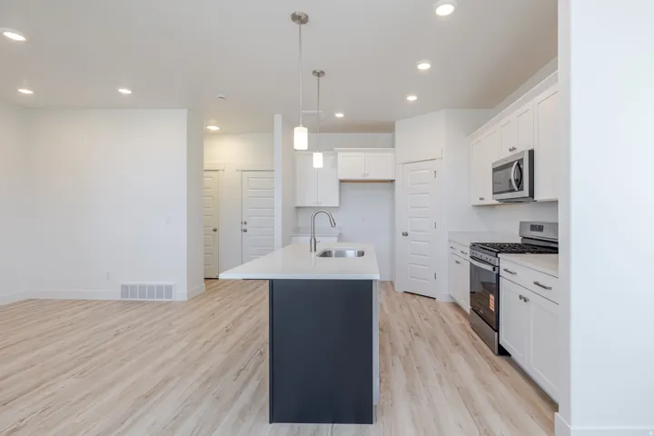 Open-concept kitchen with a central island, stainless steel appliances, white cabinetry, and light wood-finish flooring