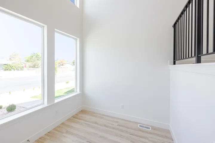 Soaring ceiling height with high-level window, multiple large windows, wood-finish flooring, and a black metal railing