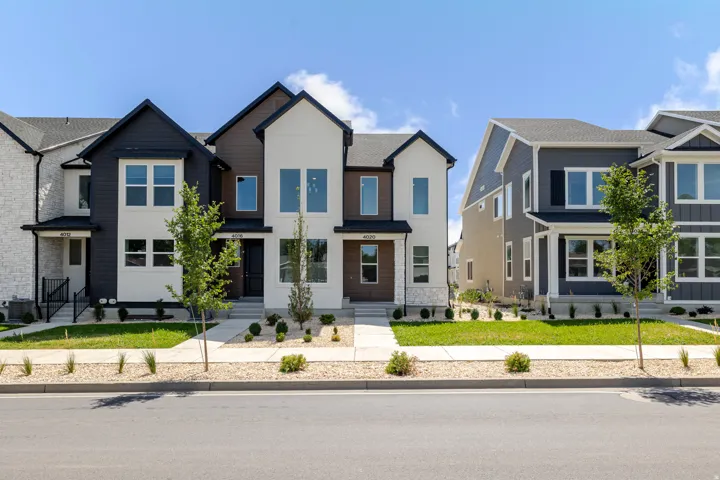 Modern townhome exterior featuring multi-toned siding, a distinct gabled roofline, and established landscaping with mature trees
