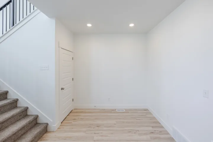 Recessed lighting, wood-finish flooring, white walls, built-in staircase with carpeted treads, and a paneled door