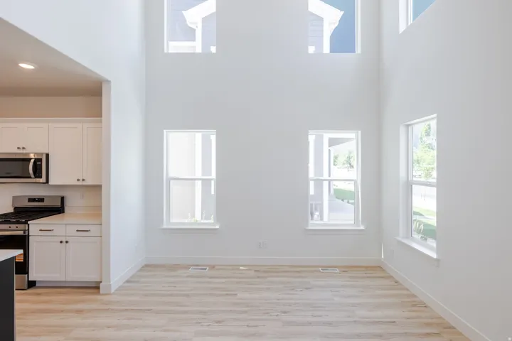 Soaring ceilings, abundant natural light from multiple windows, wood-finish flooring, and a kitchen with white cabinetry and stainless steel appliances
