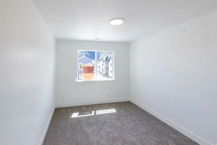 White walls, gray carpeting, a single window, and an overhead flush-mount light fixture