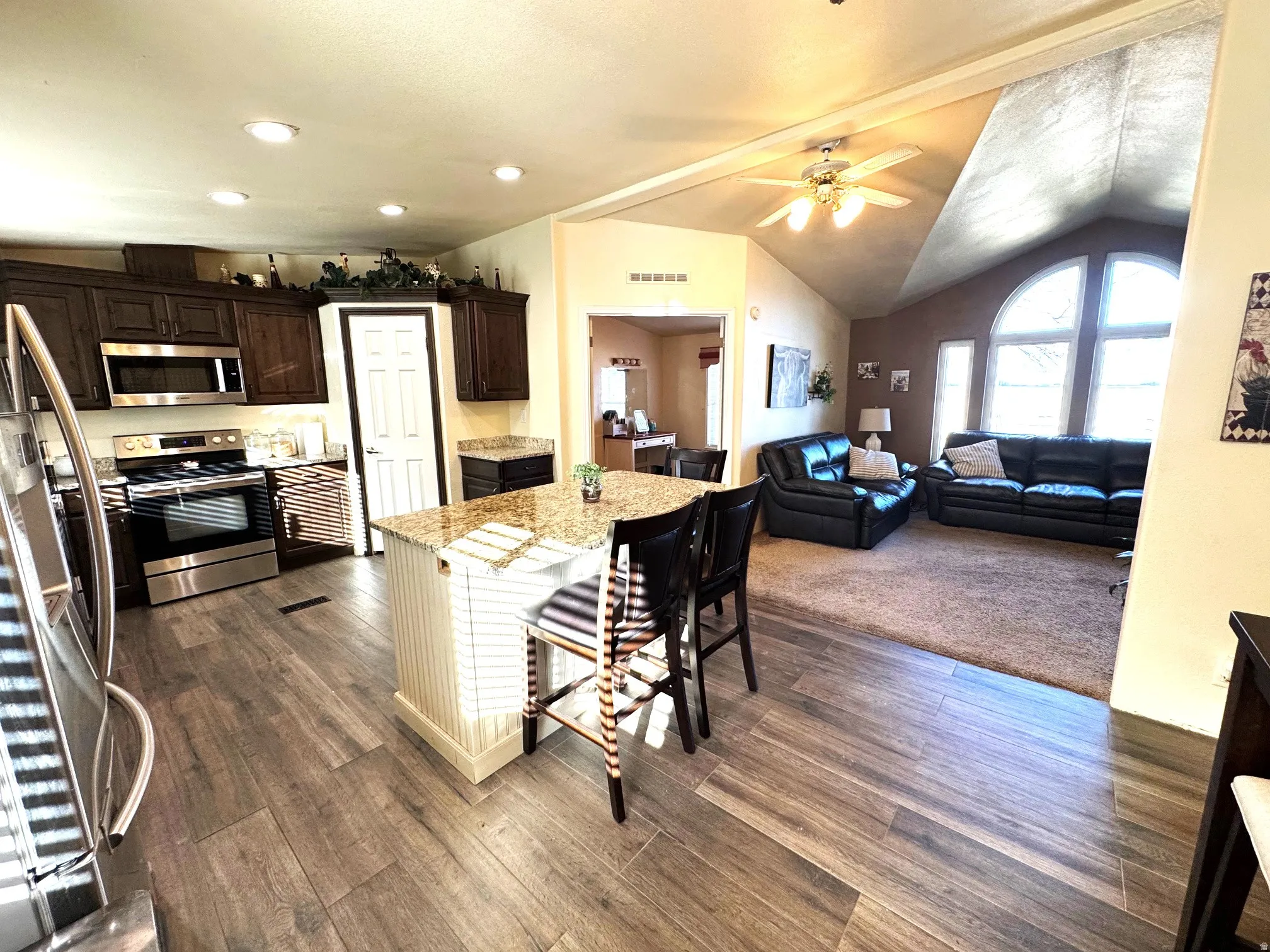 Dual tone kitchen with stainless steel appliances, two tone color scheme, light stone counters, a breakfast bar, and a ceiling fan