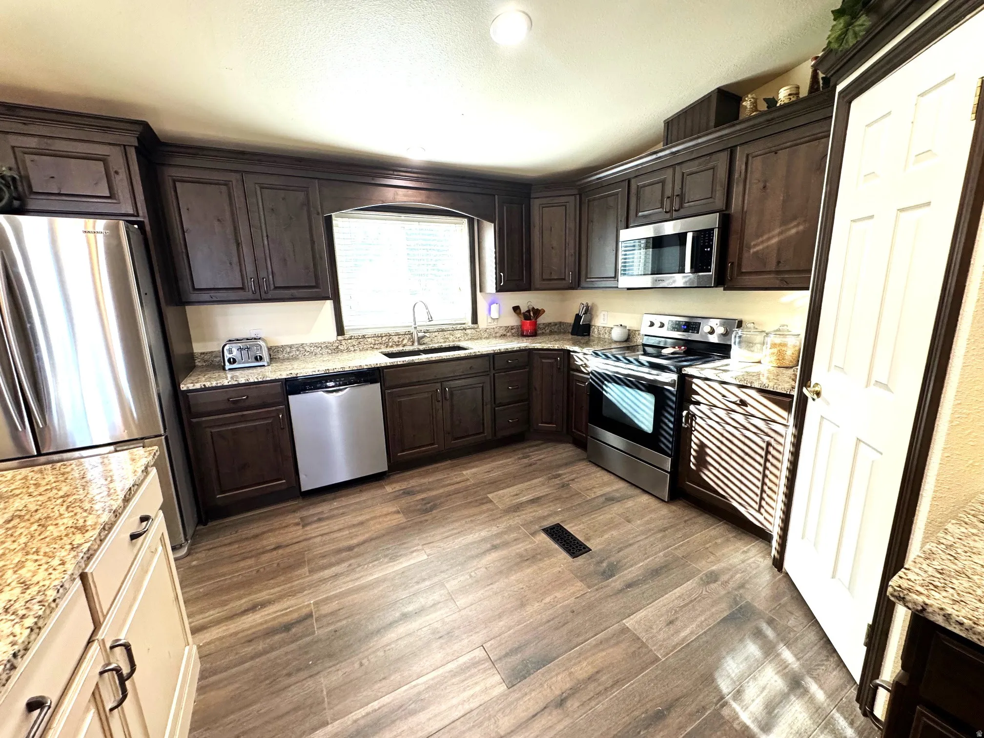 Kitchen with dark wood finish cabinetry, stainless steel appliances, light stone countertops, and dark wood finished floors
