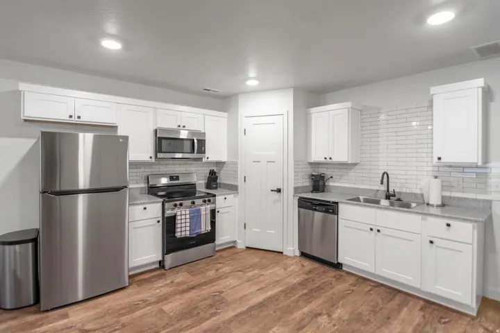 Kitchen with stainless steel appliances, white cabinets, dark wood finished floors, tasteful backsplash, and light stone countertops
