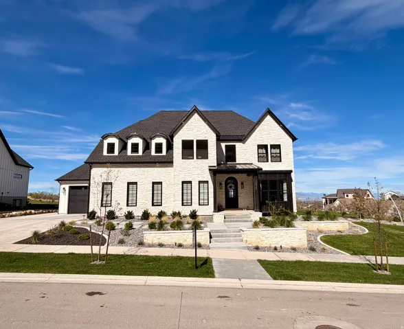 French country-inspired facade with stacked stone siding, a shingled roof, concrete driveway, an attached garage, side parking, and a front lawn