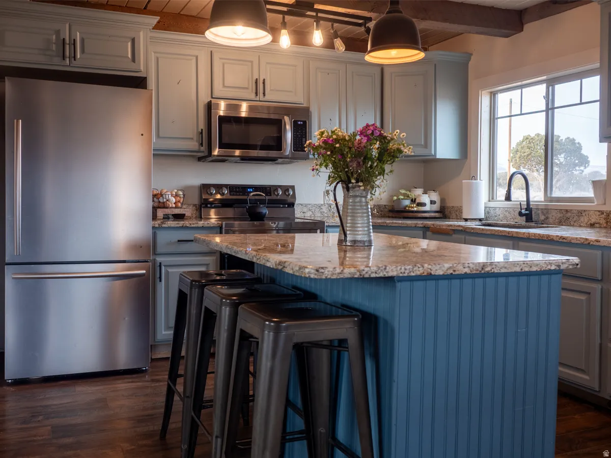 Kitchen featuring stainless steel appliances, a center island, a breakfast bar, light stone countertops, and beamed ceiling