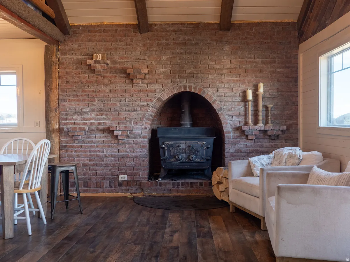 Living area featuring dark wood-style floors, a wood stove, a wooden ceiling with exposed beams, and wooden walls