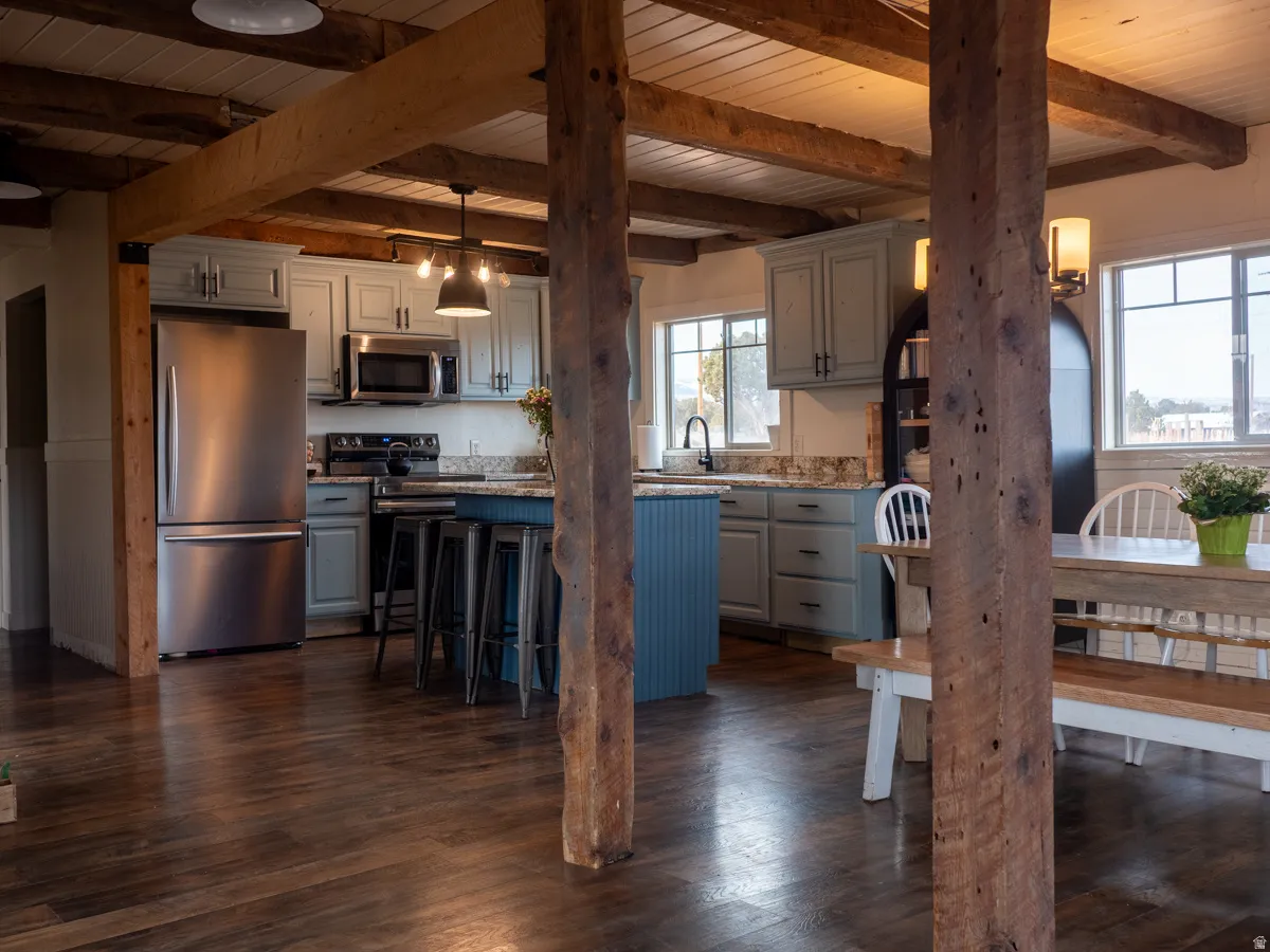 Two tone kitchen featuring stainless steel appliances, a center island, dark wood-type flooring, a wood ceiling with exposed beams, and a breakfast bar area