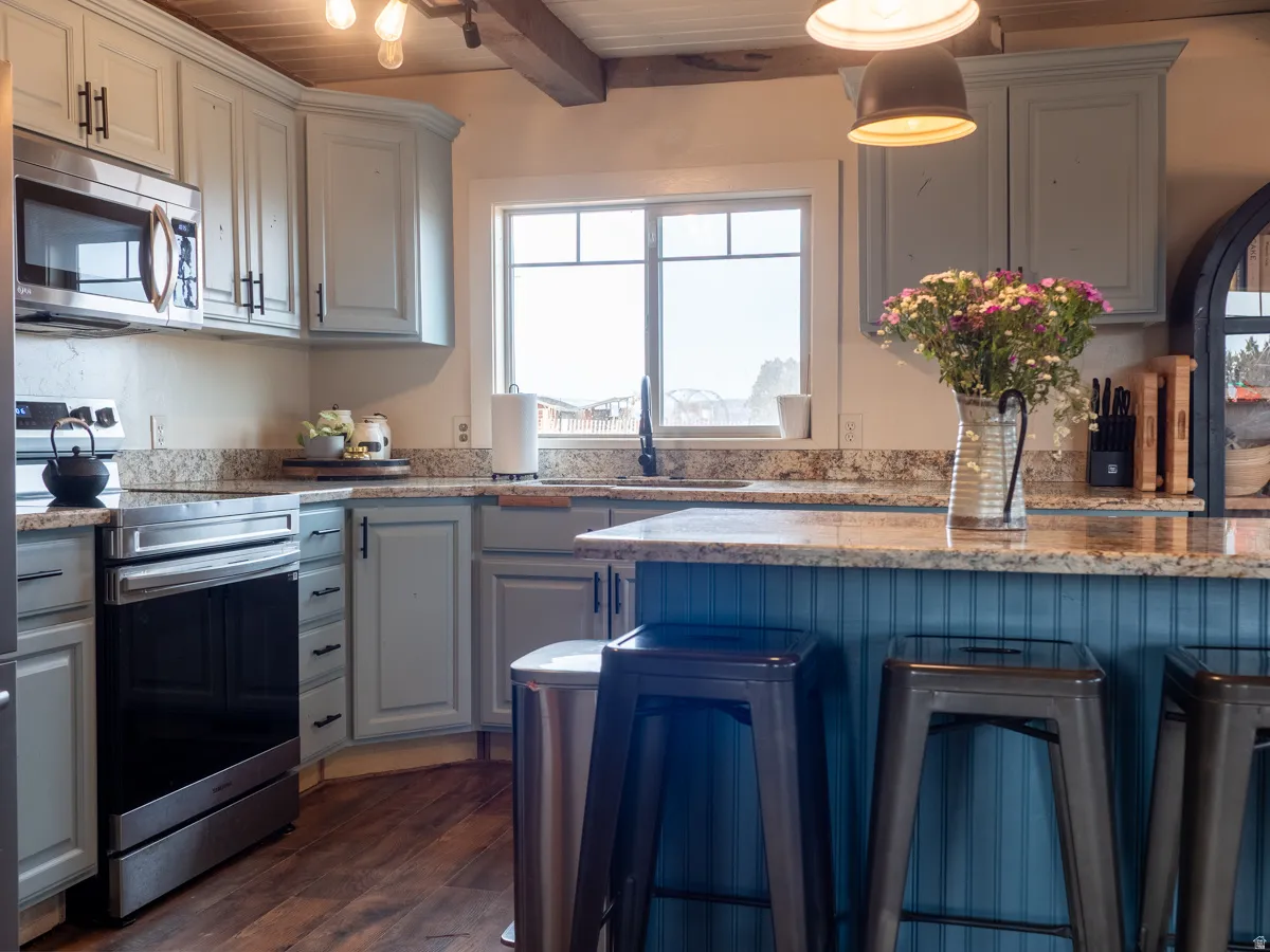 Kitchen with stainless steel appliances, a wooden ceiling with exposed beams, light stone countertops, dark wood-style flooring, and a kitchen bar