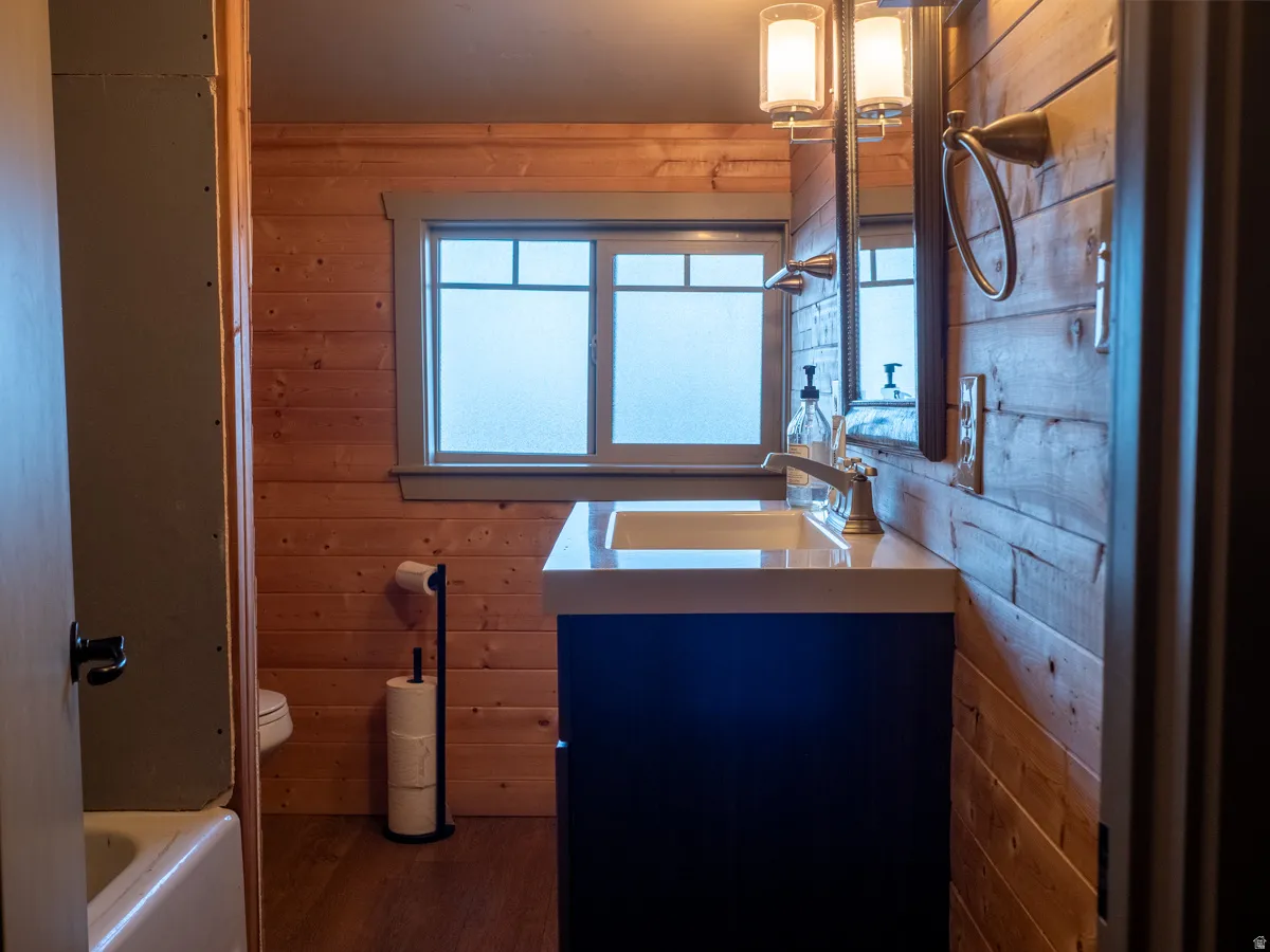 Bathroom featuring vanity, wooden walls, dark wood-style floors, and a bath
