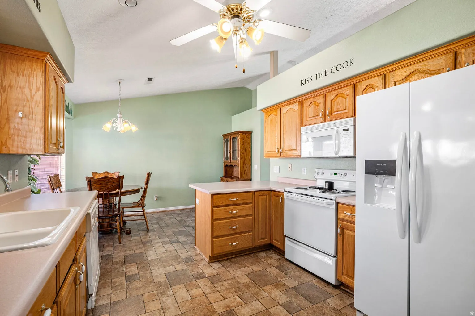 Kitchen  has lots of cabinets for storage with  white appliances, light countertops, a peninsula, a ceiling fan,