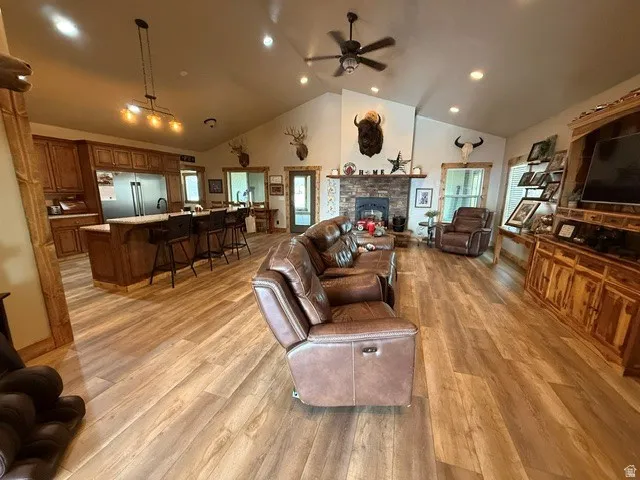 Living area featuring ceiling fan, a high ceiling, a stone fireplace, light wood-type flooring, and recessed lighting