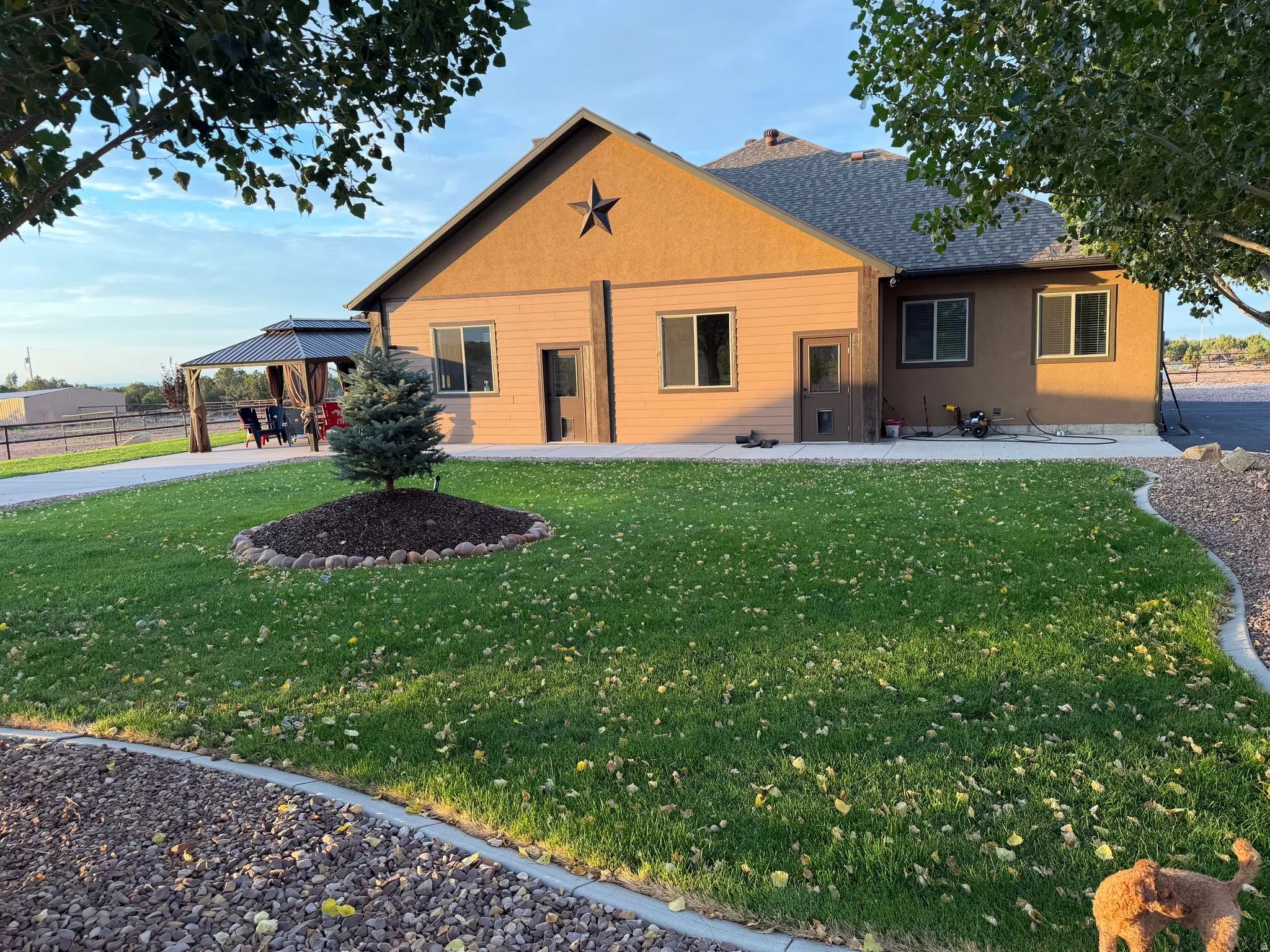 Stucco exterior with a gable roofline, featuring a decorative star accent, multiple windows, and a paved patio area