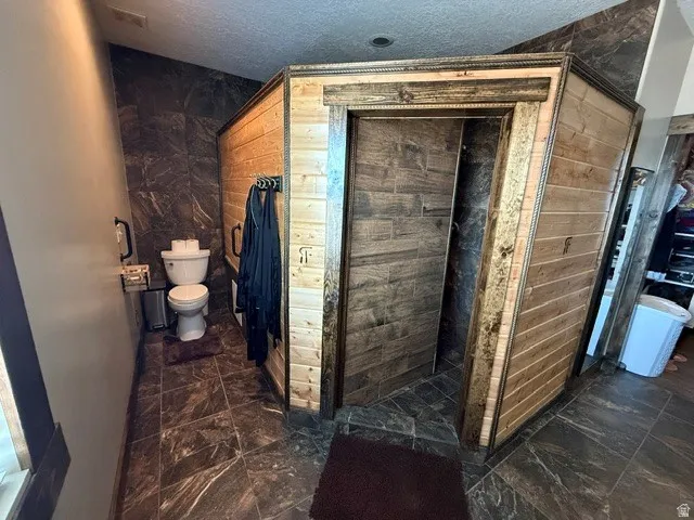 Bathroom with a textured ceiling, dark marble finish flooring, and a shower stall