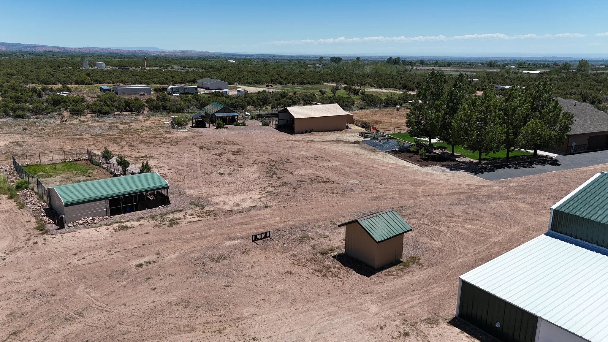 Expansive property featuring multiple outbuildings, including a large barn with a green metal roof, a smaller utility shed, and a covered structure with an open side