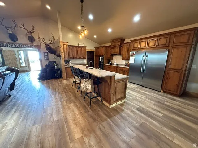 Kitchen with wood finish cabinets, a kitchen breakfast bar, built in fridge, vaulted ceiling, and a spacious island