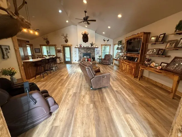Living room with light wood finished floors, ceiling fan, a high ceiling, a stone fireplace, and recessed lighting