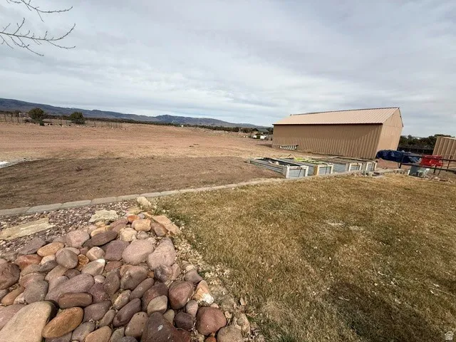 View of green lawn featuring a vegetable garden, an outbuilding, a mountain view, and a view of countryside
