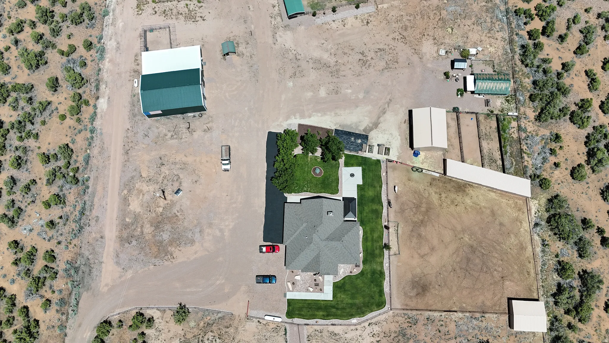 Expansive property featuring a central residence with a surrounding lawn, multiple accessory structures, fenced areas, and an unpaved driveway