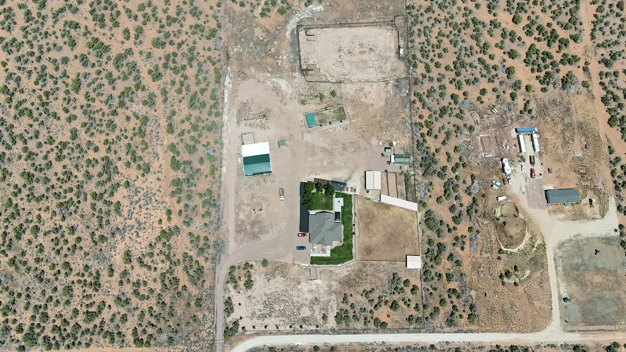 Expansive property featuring a central residence with a manicured lawn, multiple outbuildings including a large green-roofed structure, unpaved access roads, and natural desert landscaping
