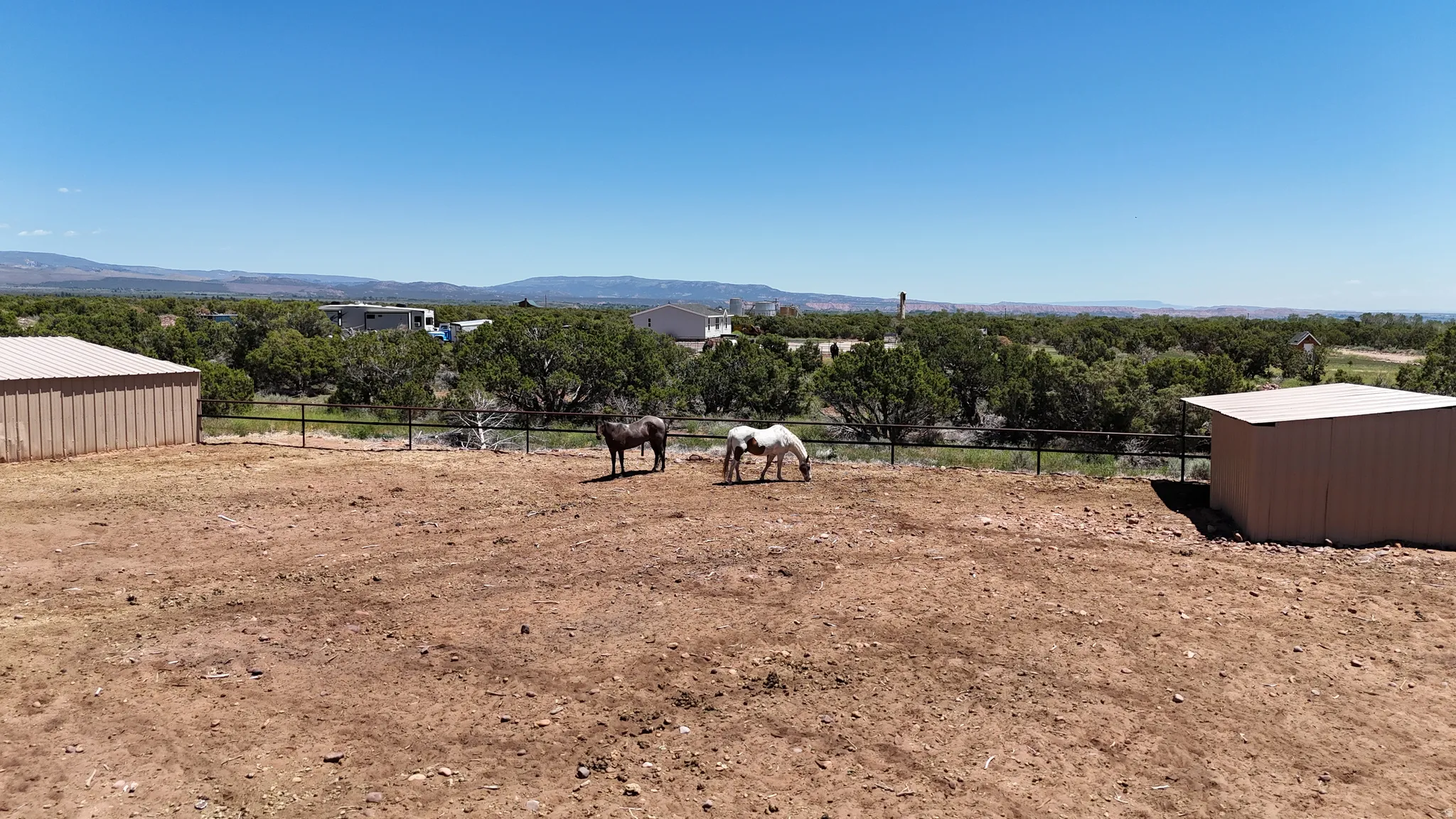 Expansive fenced paddock with two metal sheds and distant mountainous terrain
