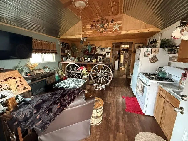 Kitchen featuring white appliances, dark wood-style flooring, wood walls, and a vaulted wood ceiling
