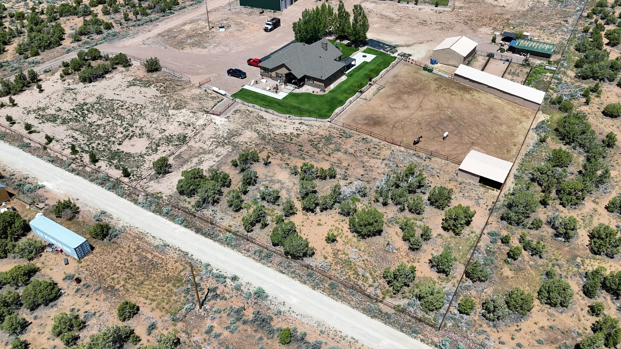 Expansive property featuring a ranch-style residence with a manicured lawn, an outdoor riding arena, multiple outbuildings, and a gravel driveway