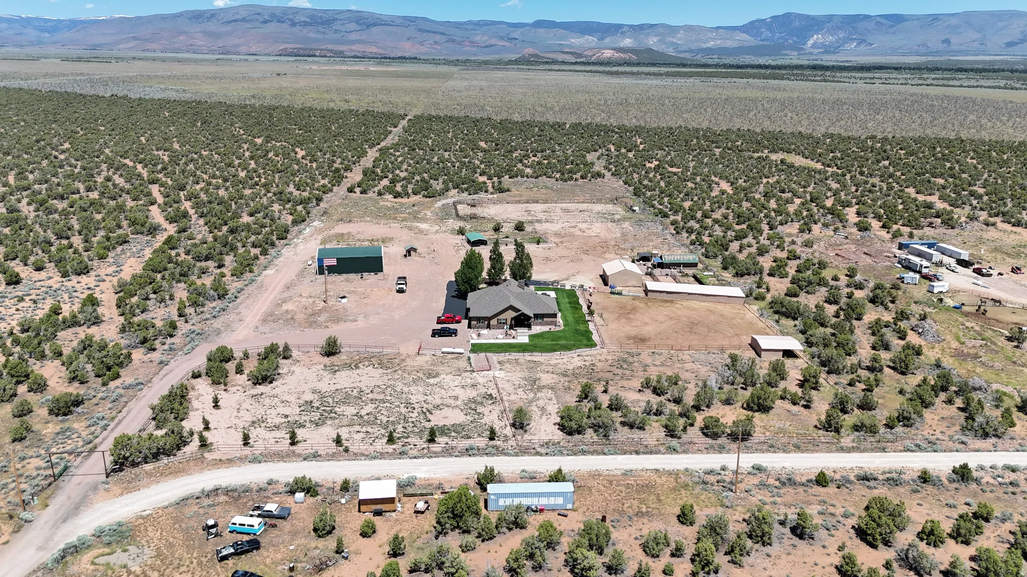Expansive property featuring a single-story residence with a green lawn, multiple outbuildings, and an unpaved access road