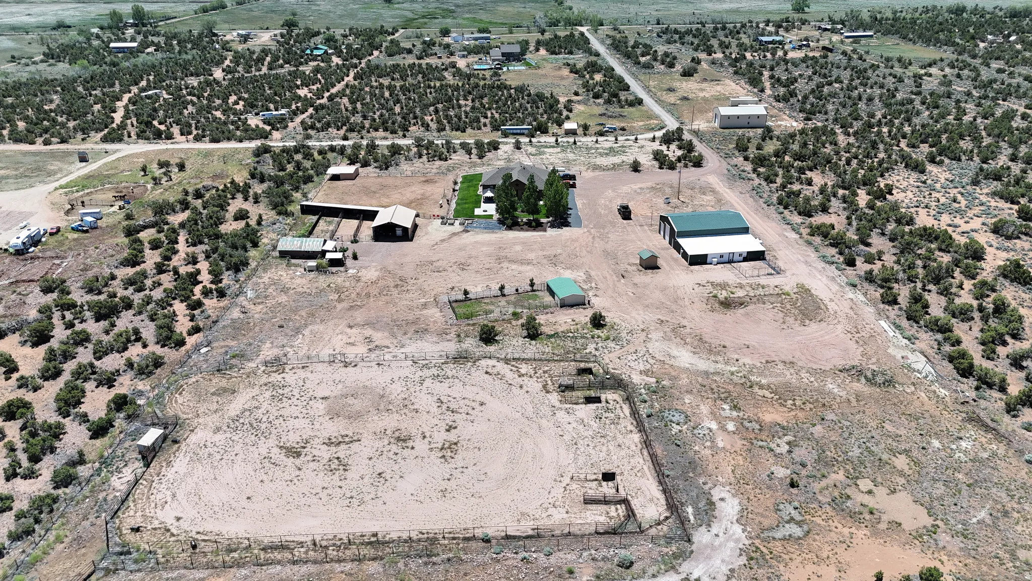 Expansive rural property featuring a main residence with a manicured lawn, multiple outbuildings, a large metal-sided workshop with a green roof, and a fenced equestrian arena