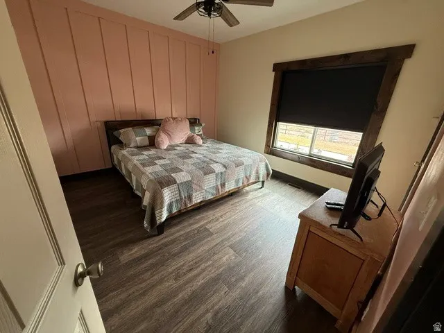 Bedroom featuring a ceiling fan, a decorative wall, and dark wood-type flooring