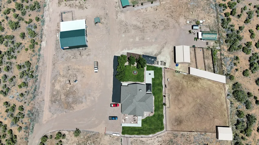 Expansive property featuring a central residence with a surrounding lawn, multiple accessory structures, fenced areas, and an unpaved driveway
