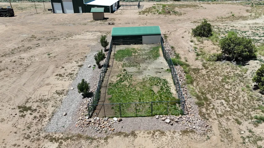 Fenced enclosure featuring a green-roofed shelter, partial vegetation, and surrounding gravel and rock landscaping