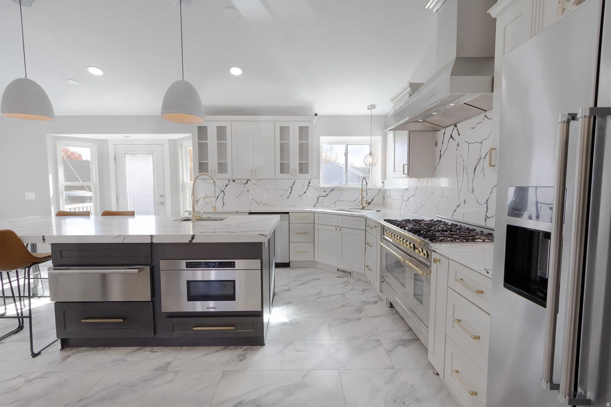 Dual tone kitchen with high end appliances, light stone countertops, decorative light fixtures, a kitchen island with sink, and glass fronted cabinets